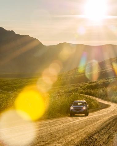 A driver cruises down the highway under the midnight sun
