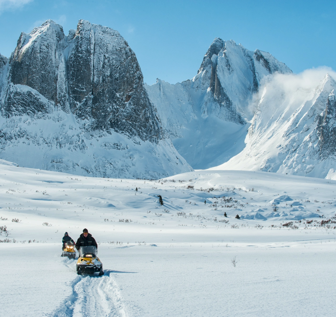 Two people on snowmobiles with mountains in the background