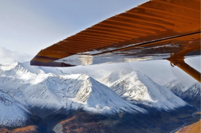 The wing of an airplane with snowy mountains in the background