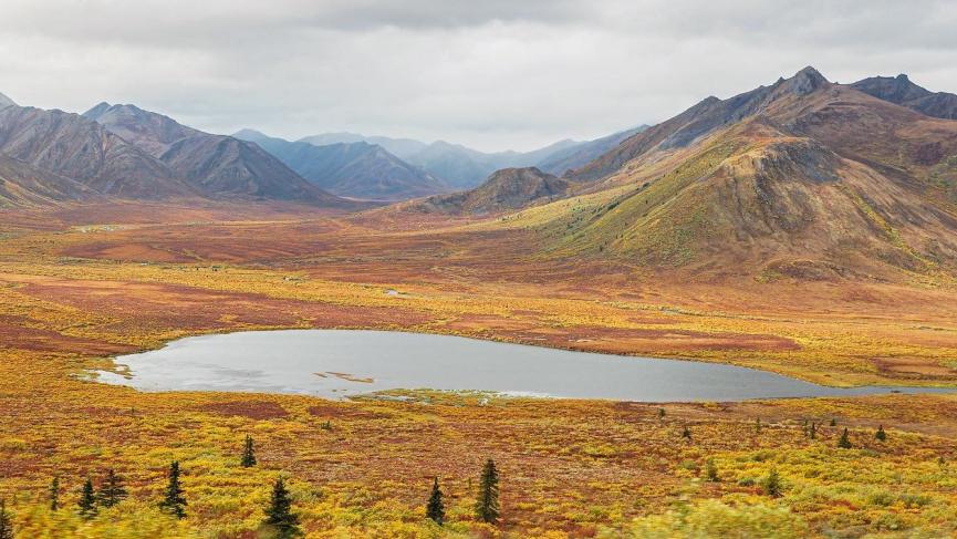 A lake is surrounded by autumn brush. Mountains stretch tall in the distance.