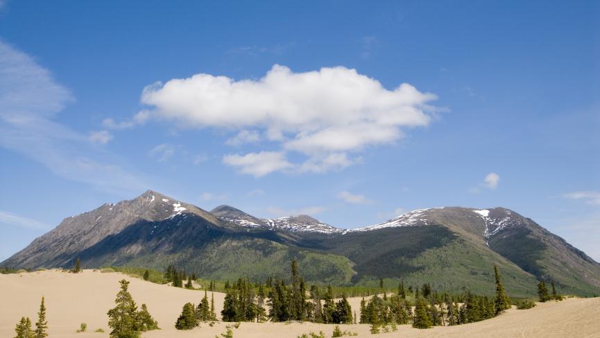 Sand dunes spread across the base of a mountain under a bright blue sky