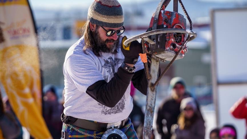 A bearded man wearing a beanie focuses, preparing to throw a red chainsaw