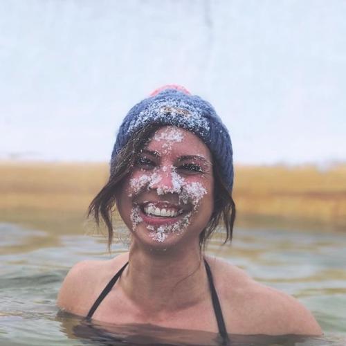 A woman in a hot spring smiles with snow on her face