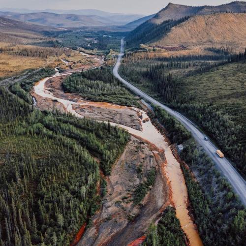 Cars drive along the Dempster highway next to a river