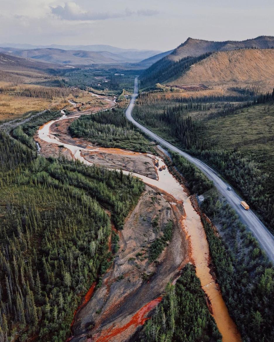 Cars drive along the Dempster highway next to a river 