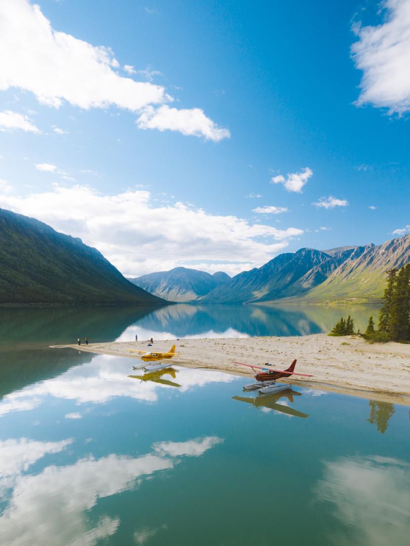 Two float planes are docked along the shore of a pristine blue lake