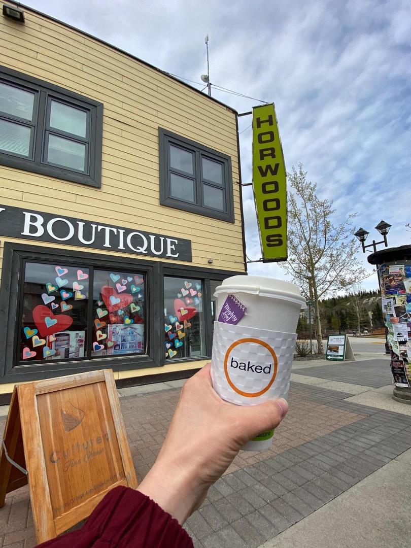 POV style photo of a person holding a coffee cup in front of corner shops downtown