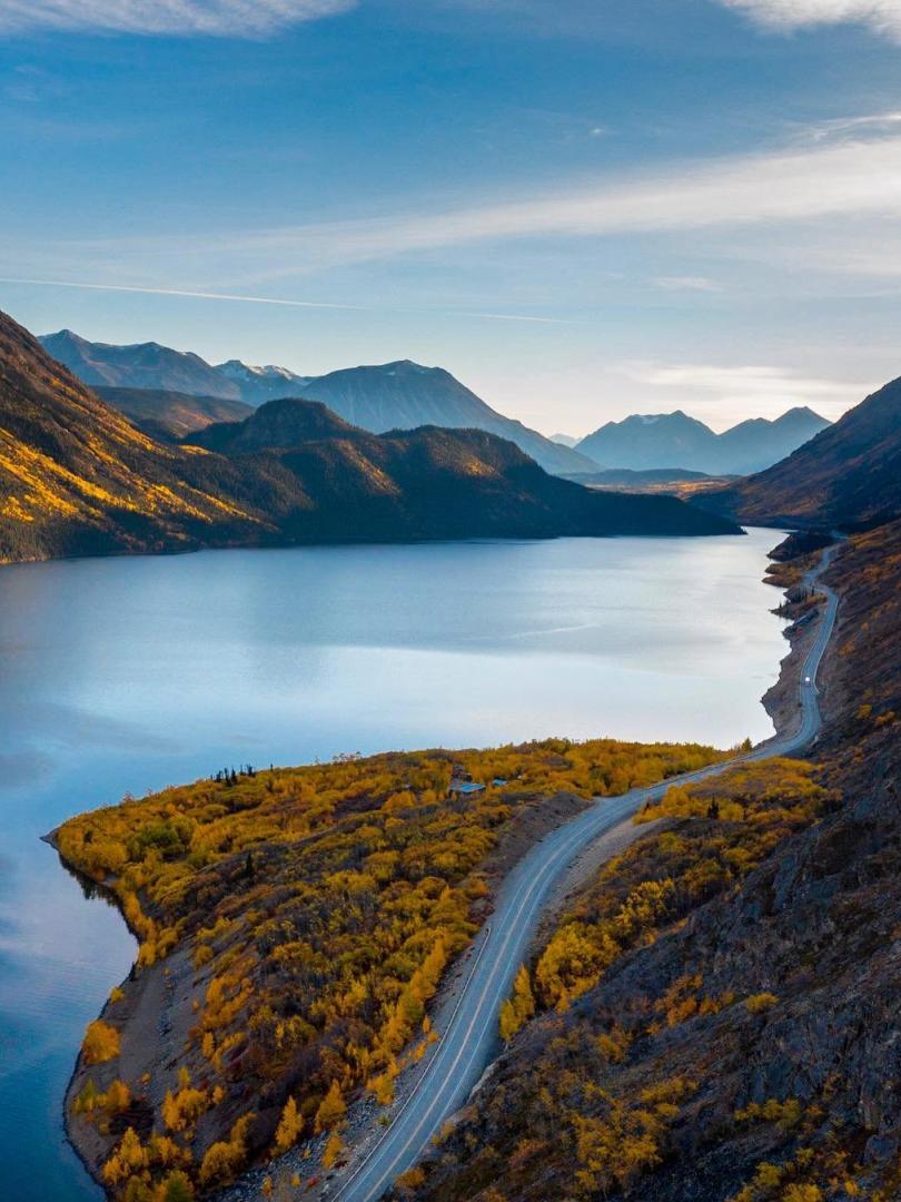 A road winds alongside a large lake towards a mountain range