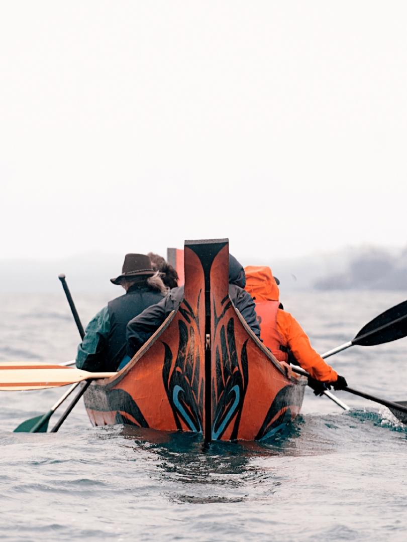 People in a traditional indigenous canoe paddle on a lake on a smoky day