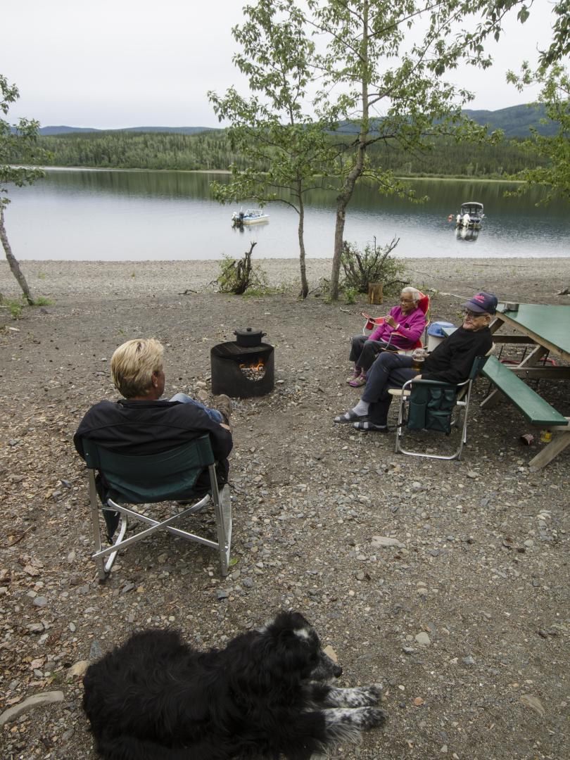 Campers gather around a fire pit with their dog