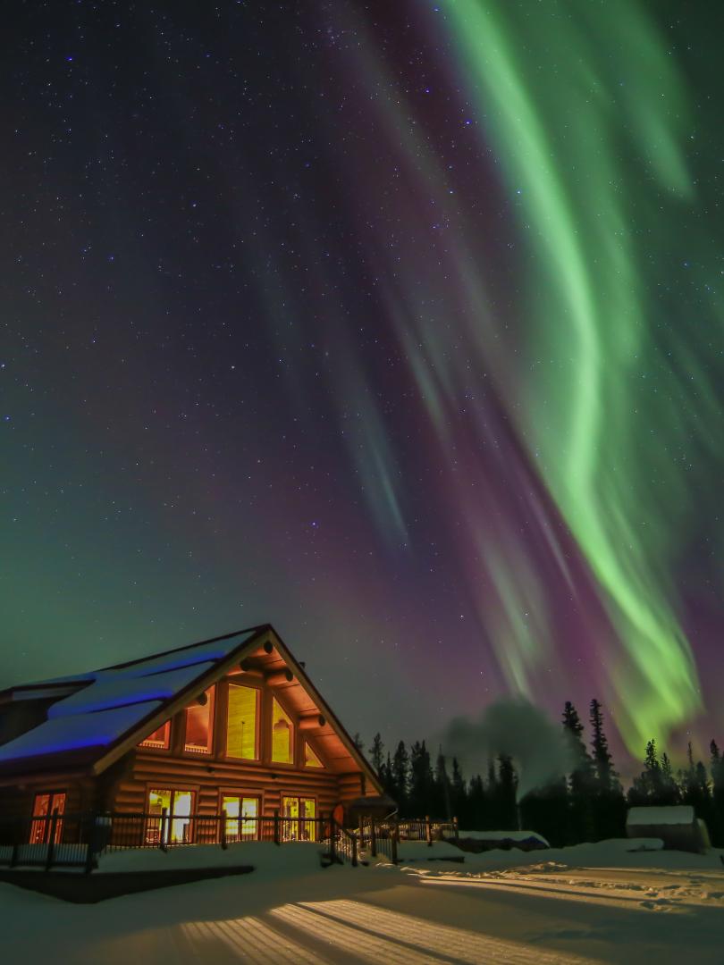 Green and purple northern lights above a wood lodge in the winter