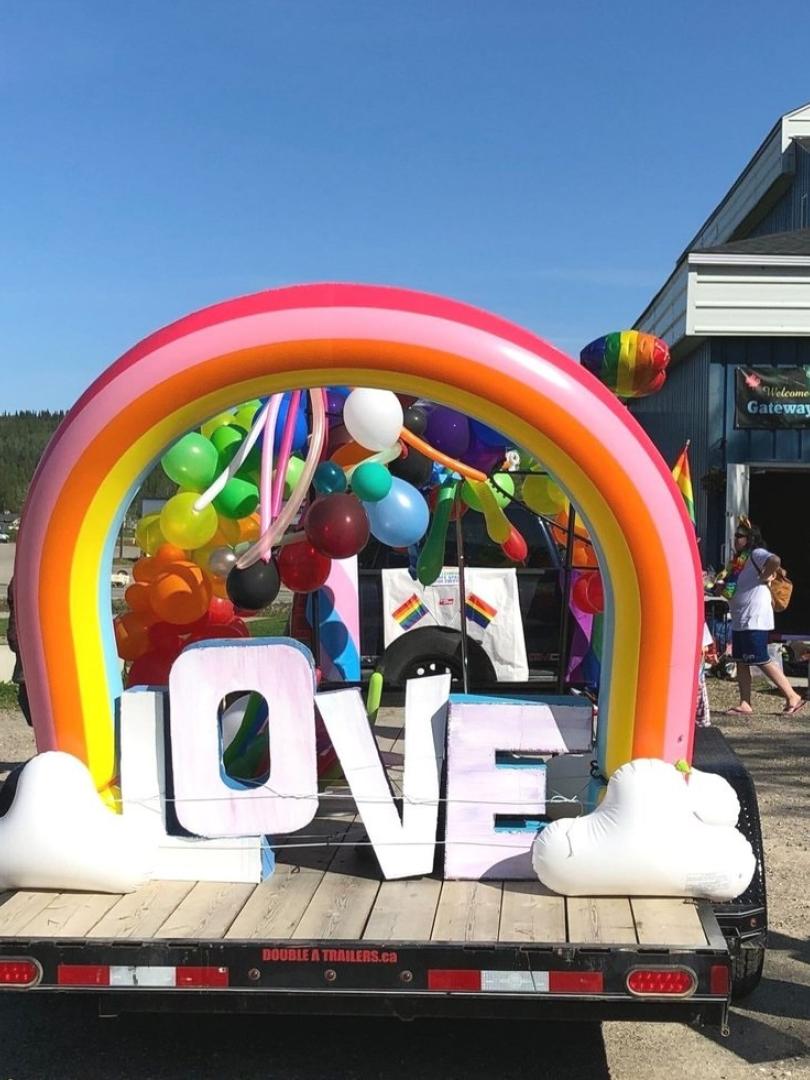 Rainbow on a trailer, with the wordl love written under it and people walking around