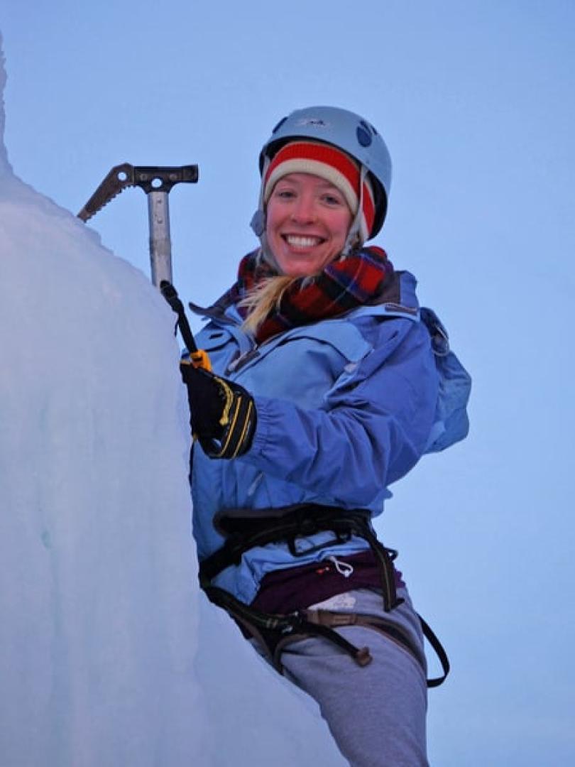 Smiling woman in blue giving ice climbing a try