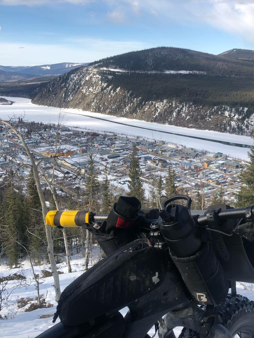 Fat bike standing at the top of the Midnight Dome with a view of Dawson City and the river