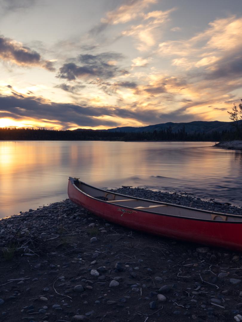 empty canoe at shore of Yukon River with the sun setting in background