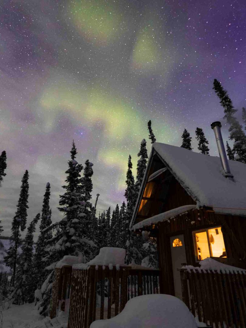 Evening winter scenery with a cabin and Aurora Borealis above