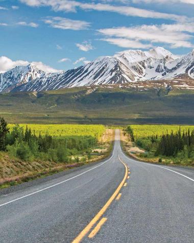 Alaska highway with snow-capped mountains on the horizon