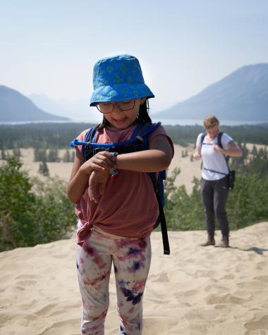 A child looks at their watch at the top of a sand dune in the Carcross Desert.