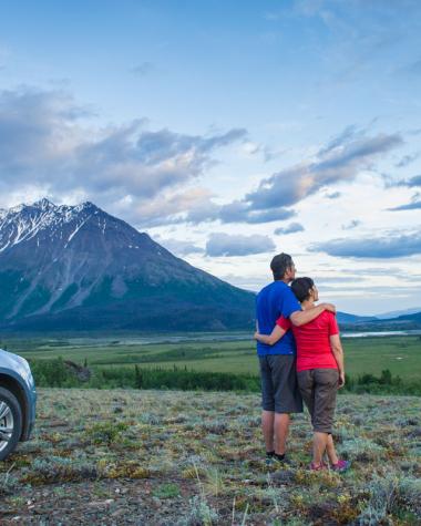 A couple takes in a mountain view next to their SUV